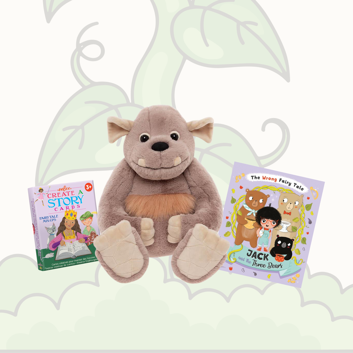 A plush gray monster toy sits centered between two children's books on a pale green illustrated background. The left book is titled 'Create Your Story Cards' and the right book is titled 'The Wrong Fairy Tale: Jack and the Black Cat'.