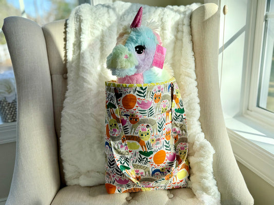 Stuffed unicorn toy with a colorful patchwork bag on a white chair