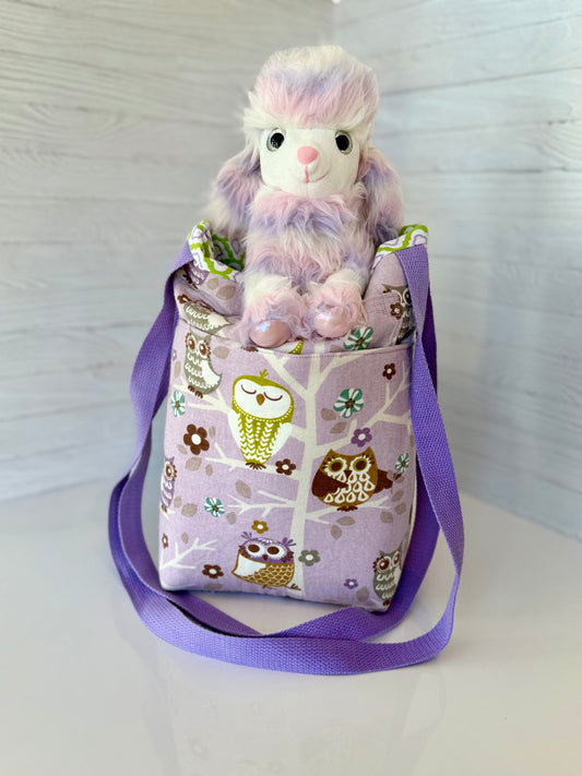 Purple bag with owl pattern containing a plush toy on a white background