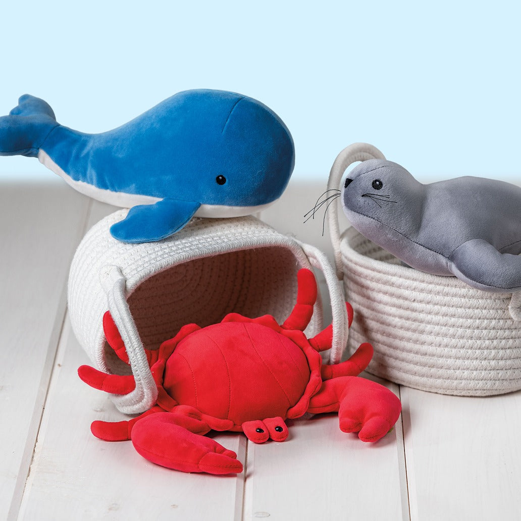 Plush toys including a blue whale, red crab, and gray seal on a light wooden floor.