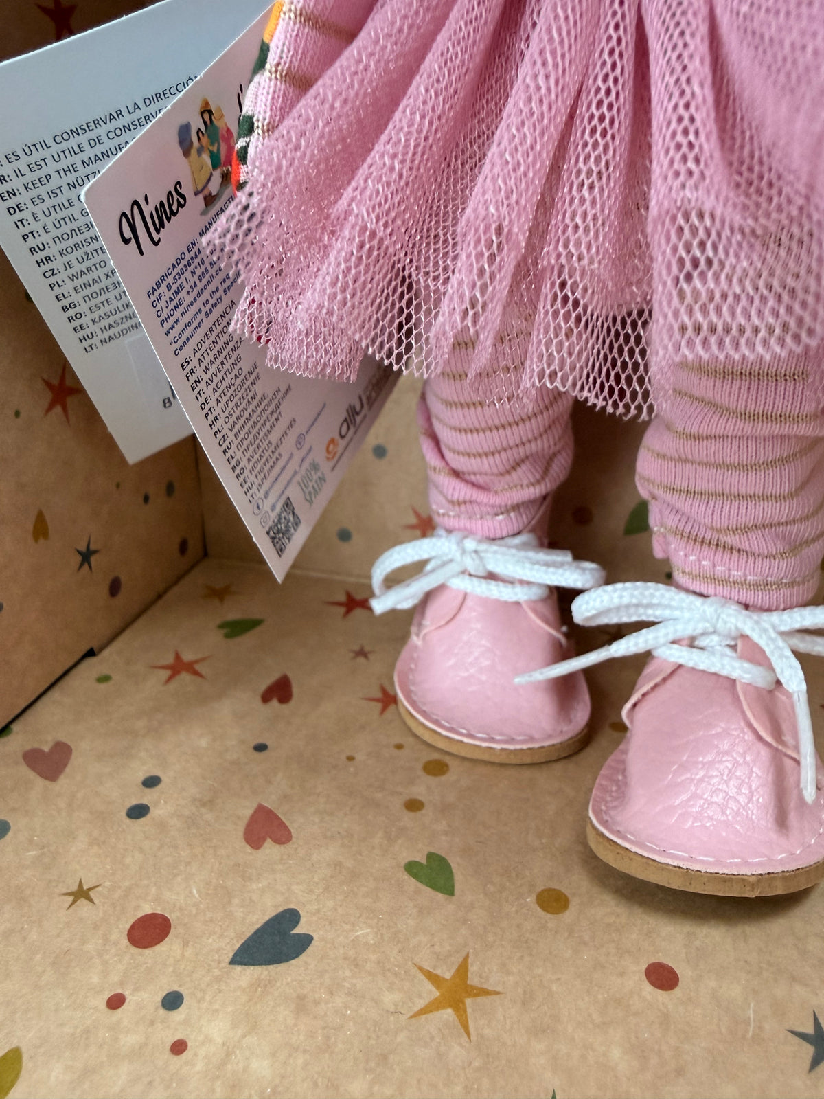 Close-up of the pink and tan striped tights under a mauve layered crinoline "tutu" type skirt with pink leatherette shoes, worn by a 9" doll named Little Pippa Pink Wool handmade by Nines d'Onil. She stands in a star patterned display box which is open at the front.