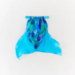 A sheer mermaid tail skirt in vibrant blue and green with a purple scale pattern and a matching blue elastic waistband, laid flat on a white background.